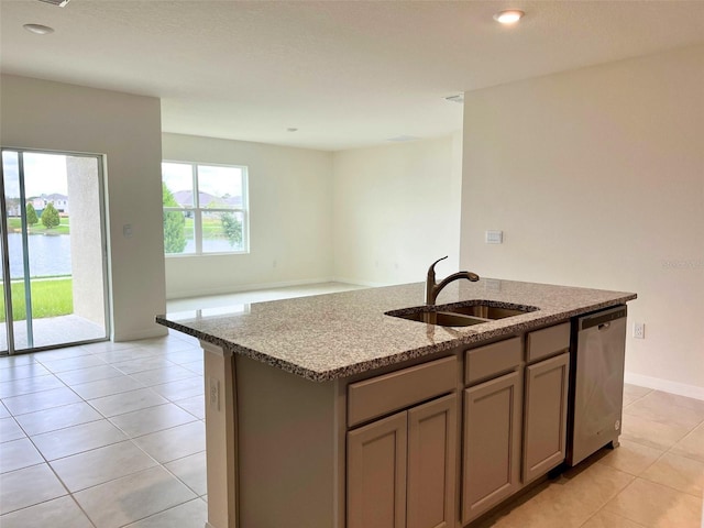 kitchen with sink, dishwasher, light stone counters, an island with sink, and light tile patterned flooring