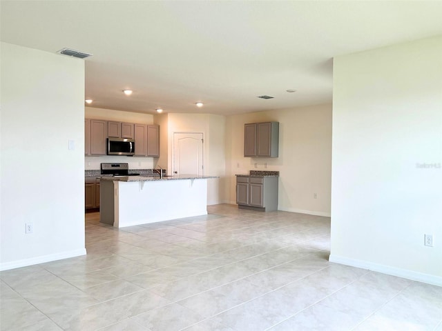 kitchen with sink, a kitchen bar, a kitchen island with sink, light stone counters, and stainless steel appliances