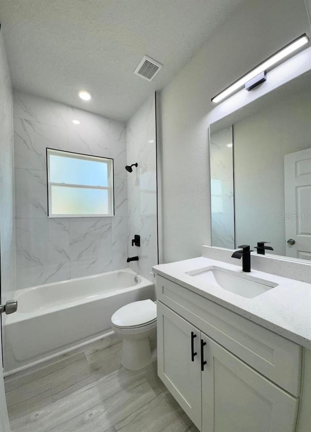 full bathroom with hardwood / wood-style floors, vanity, a textured ceiling, tiled shower / bath, and toilet