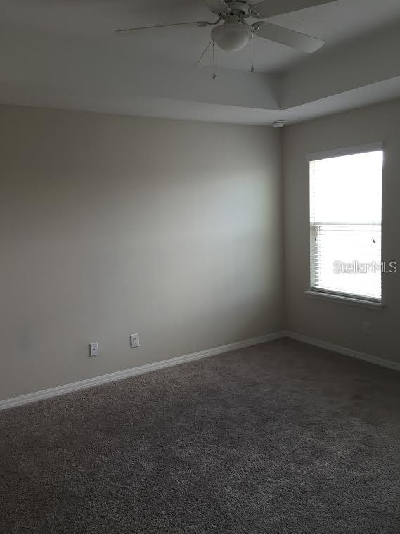 spare room featuring ceiling fan and dark carpet