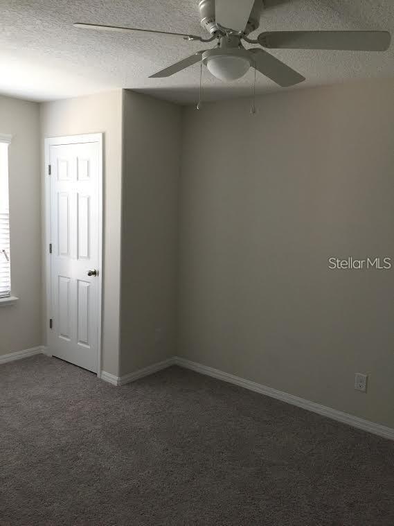 empty room featuring dark colored carpet, ceiling fan, and a textured ceiling