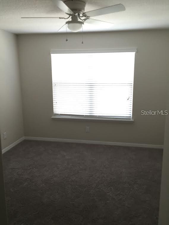 empty room with dark colored carpet, a healthy amount of sunlight, and ceiling fan