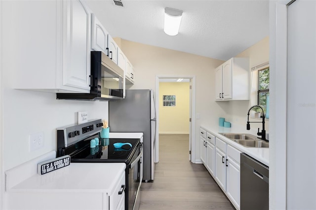 kitchen with vaulted ceiling, appliances with stainless steel finishes, sink, and white cabinets