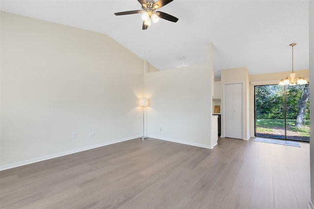 spare room with vaulted ceiling, ceiling fan with notable chandelier, and light wood-type flooring