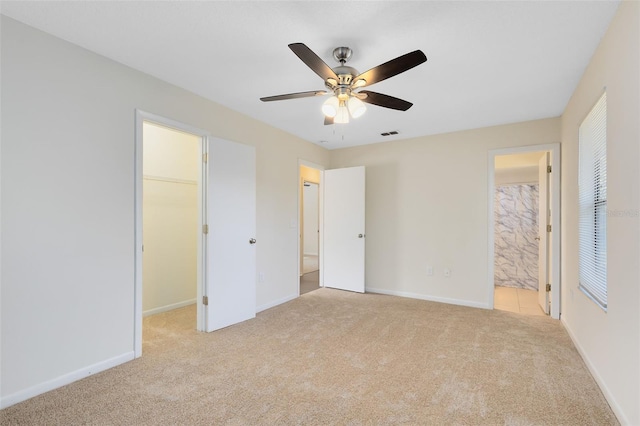 unfurnished bedroom featuring connected bathroom, a spacious closet, ceiling fan, light carpet, and a closet