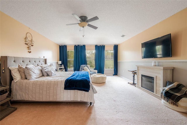 bedroom featuring visible vents, a ceiling fan, a glass covered fireplace, a textured ceiling, and carpet flooring