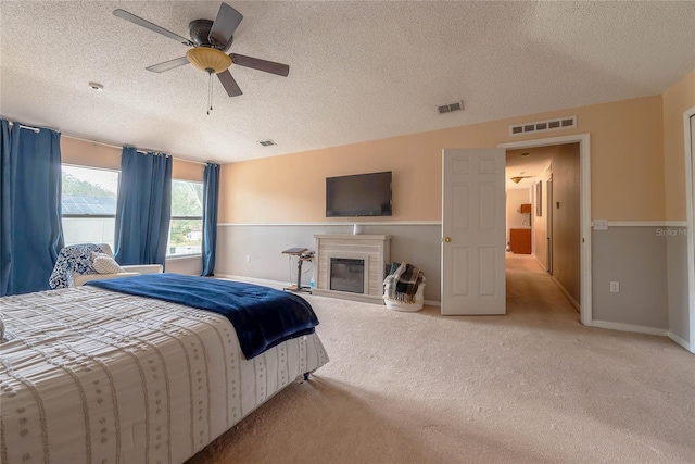 bedroom featuring a glass covered fireplace, visible vents, ceiling fan, and carpet