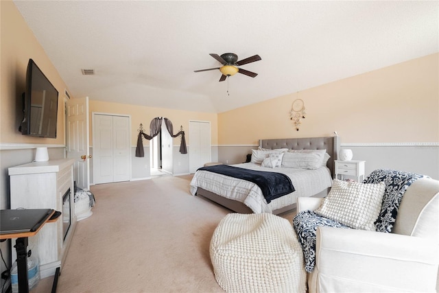 bedroom featuring visible vents, light colored carpet, lofted ceiling, ceiling fan, and two closets