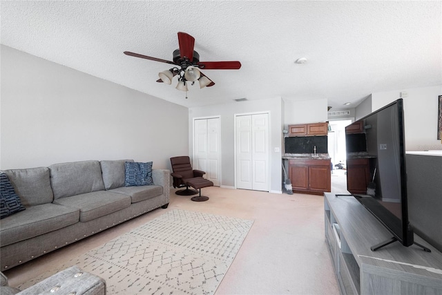 living room with a textured ceiling, light colored carpet, a ceiling fan, baseboards, and visible vents