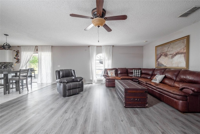 living area featuring a textured ceiling, ceiling fan, wood finished floors, and visible vents