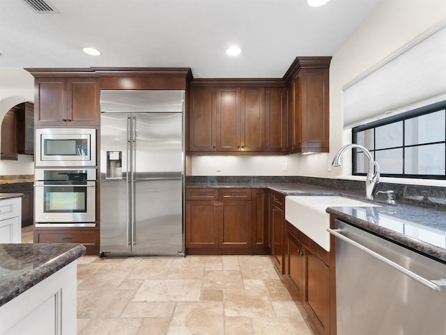 kitchen featuring dark stone counters, built in appliances, and sink