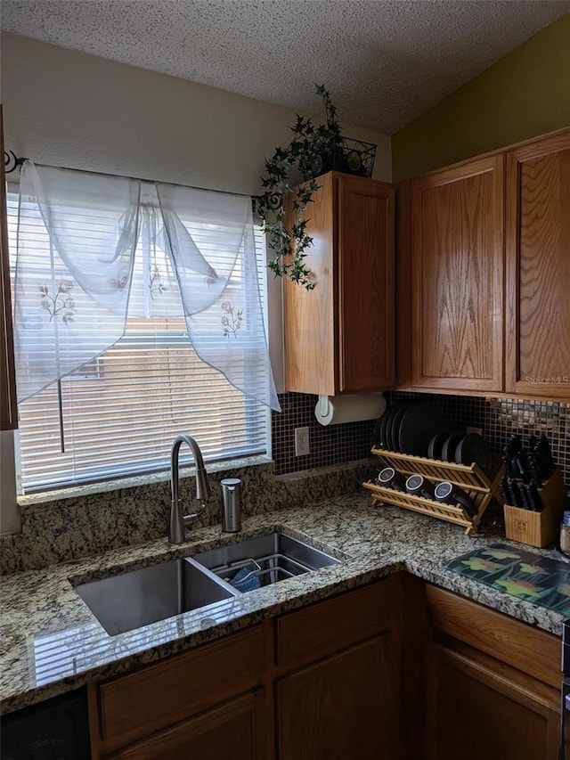 kitchen featuring sink, vaulted ceiling, a textured ceiling, stone counters, and backsplash