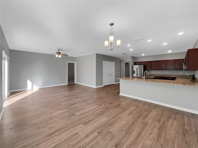 kitchen with light stone counters, stainless steel fridge with ice dispenser, light hardwood / wood-style floors, pendant lighting, and ceiling fan with notable chandelier