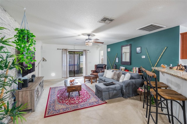 living room featuring light carpet, visible vents, ceiling fan, and a textured ceiling