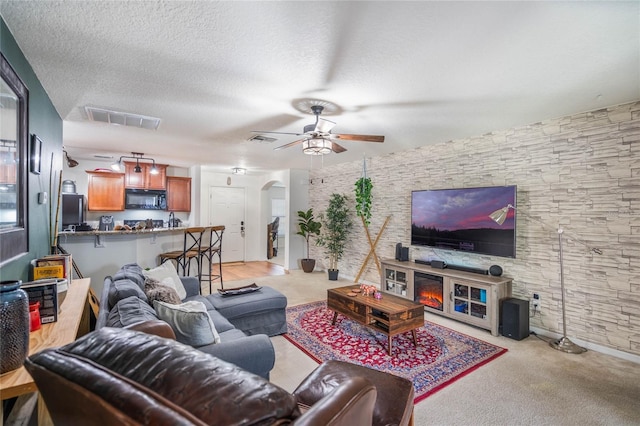 living area featuring ceiling fan, visible vents, arched walkways, and a textured ceiling