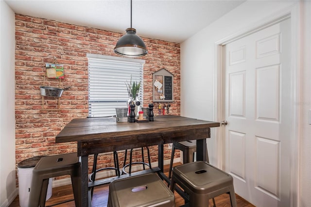 dining space with brick wall, baseboards, and wood finished floors