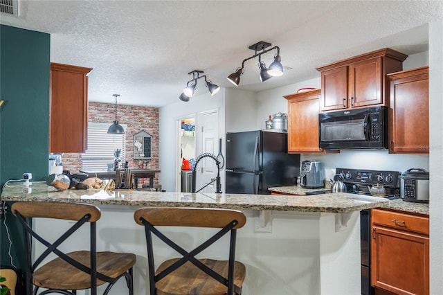 kitchen with visible vents, black appliances, a textured ceiling, a peninsula, and a kitchen breakfast bar