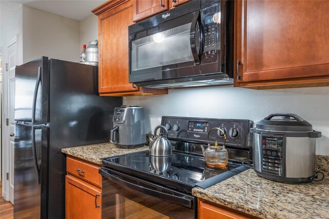 kitchen with black appliances, wood finished floors, brown cabinets, and light stone countertops