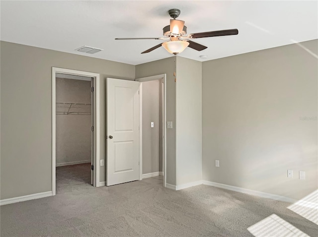 unfurnished bedroom featuring ceiling fan, light colored carpet, a spacious closet, and a closet