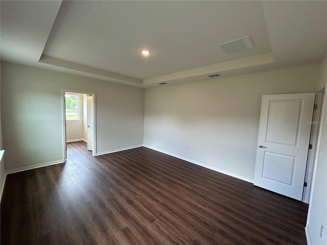 empty room featuring a raised ceiling, dark wood-style floors, baseboards, and visible vents