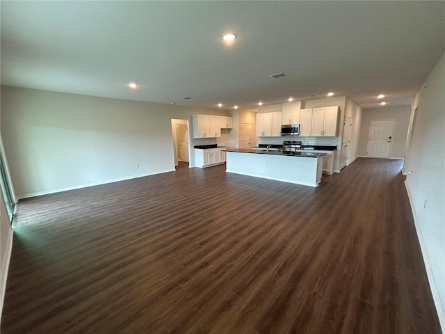 kitchen featuring white cabinetry, dark wood-style floors, open floor plan, stainless steel microwave, and dark countertops