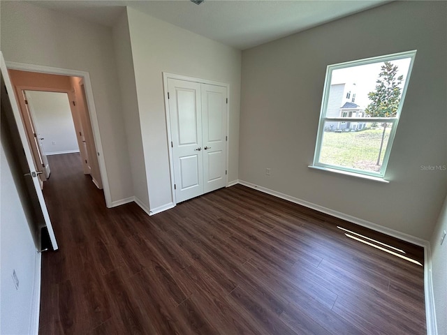 unfurnished bedroom featuring baseboards, dark wood-style flooring, and a closet