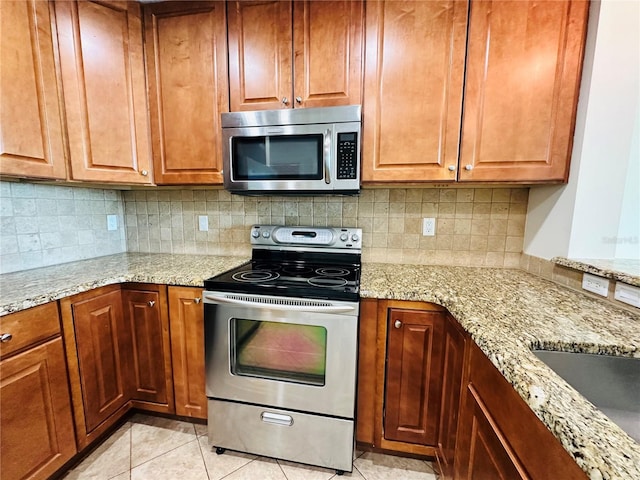 kitchen with light tile patterned floors, sink, appliances with stainless steel finishes, light stone counters, and tasteful backsplash