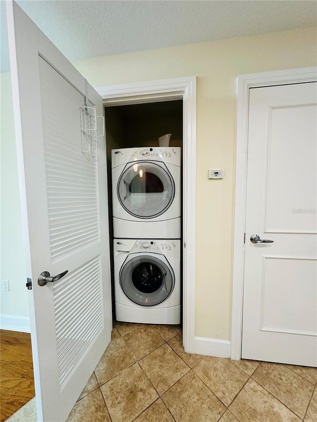 clothes washing area featuring stacked washer / drying machine, a textured ceiling, and light tile patterned floors