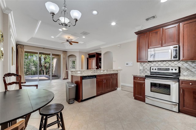 kitchen with appliances with stainless steel finishes, backsplash, hanging light fixtures, ornamental molding, and a tray ceiling