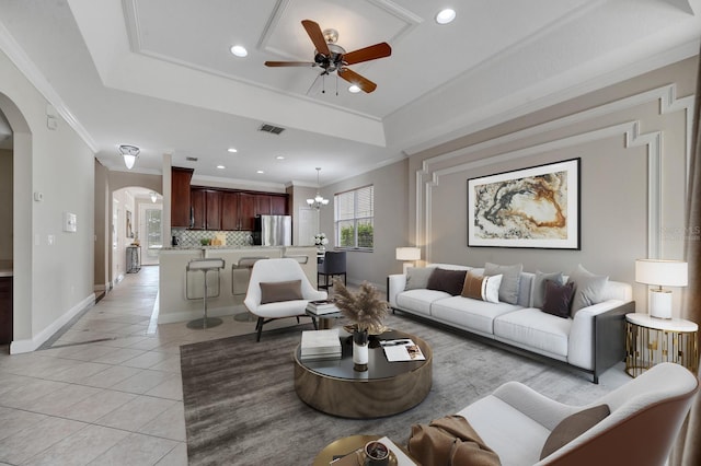 living room featuring a raised ceiling, light tile patterned flooring, ornamental molding, and ceiling fan with notable chandelier