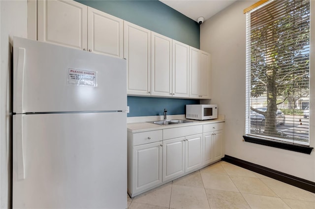 kitchen featuring white appliances, light tile patterned floors, sink, and white cabinets