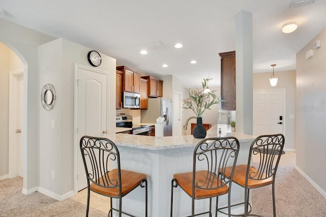 kitchen with appliances with stainless steel finishes, pendant lighting, tasteful backsplash, kitchen peninsula, and light carpet