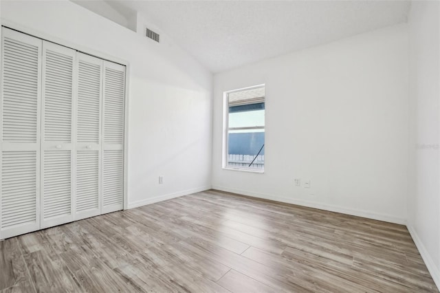 unfurnished bedroom featuring vaulted ceiling, light hardwood / wood-style floors, a closet, and a textured ceiling