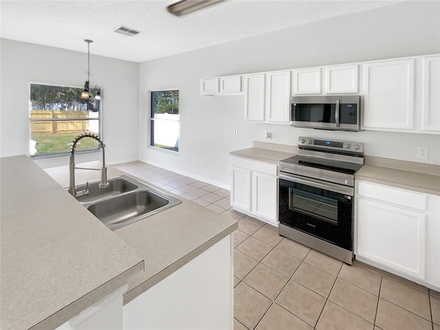 kitchen with sink, appliances with stainless steel finishes, white cabinetry, hanging light fixtures, and light tile patterned flooring