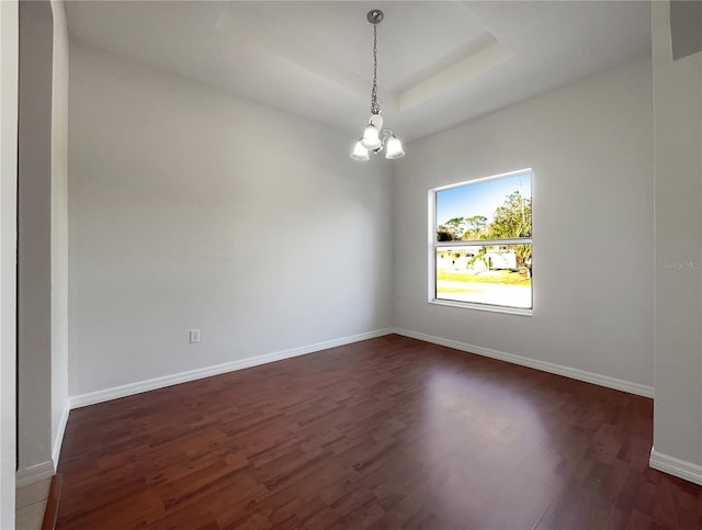 spare room featuring dark hardwood / wood-style floors, a raised ceiling, and a chandelier