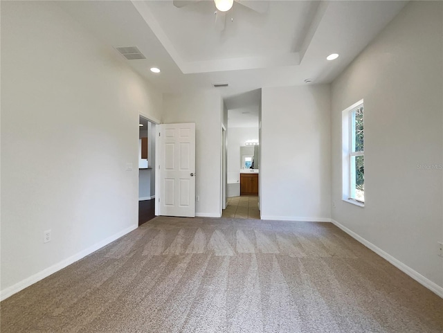 unfurnished bedroom with ceiling fan, light colored carpet, a raised ceiling, and ensuite bath