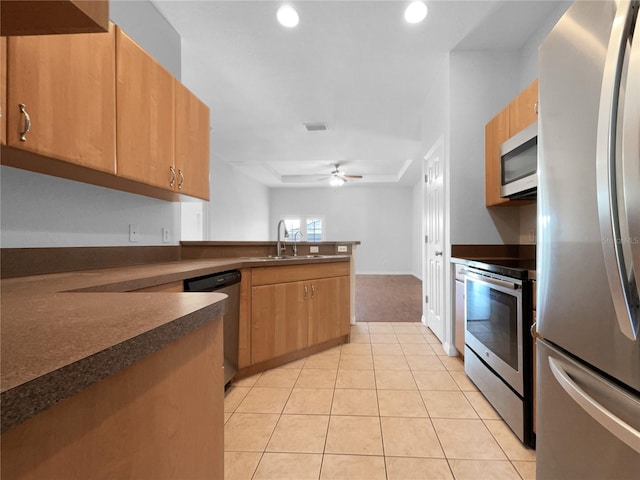 kitchen featuring sink, light tile patterned floors, ceiling fan, appliances with stainless steel finishes, and a raised ceiling