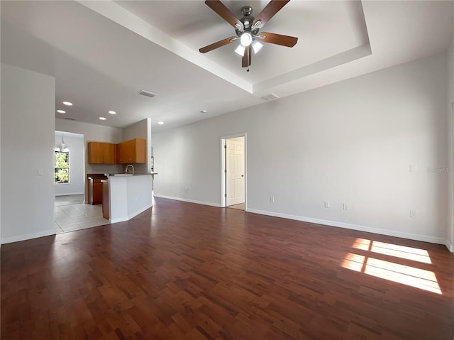 unfurnished living room with ceiling fan, a raised ceiling, and light hardwood / wood-style floors