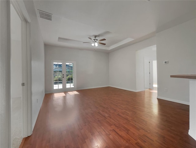 empty room with dark wood-type flooring, a raised ceiling, ceiling fan, and french doors