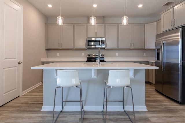 kitchen with stainless steel appliances, an island with sink, and hanging light fixtures