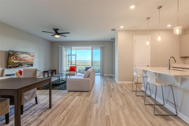 living room with ceiling fan, sink, and light wood-type flooring