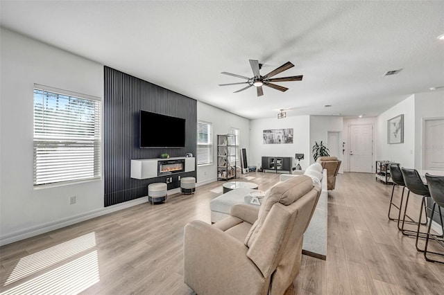 living room featuring ceiling fan, a wealth of natural light, a textured ceiling, and light hardwood / wood-style floors