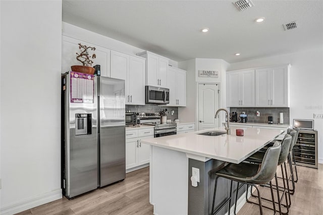 kitchen with appliances with stainless steel finishes, white cabinetry, sink, a kitchen breakfast bar, and a center island with sink