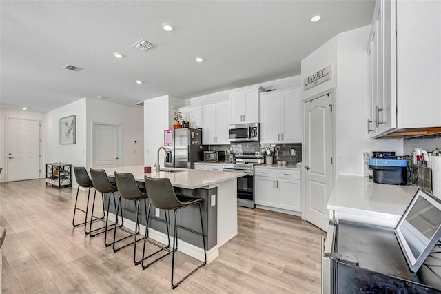 kitchen with appliances with stainless steel finishes, white cabinetry, sink, a kitchen breakfast bar, and a center island with sink