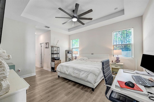 bedroom featuring ceiling fan, a tray ceiling, and light hardwood / wood-style floors