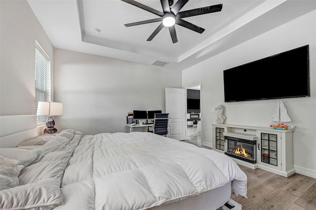 bedroom with ceiling fan, a tray ceiling, and light wood-type flooring