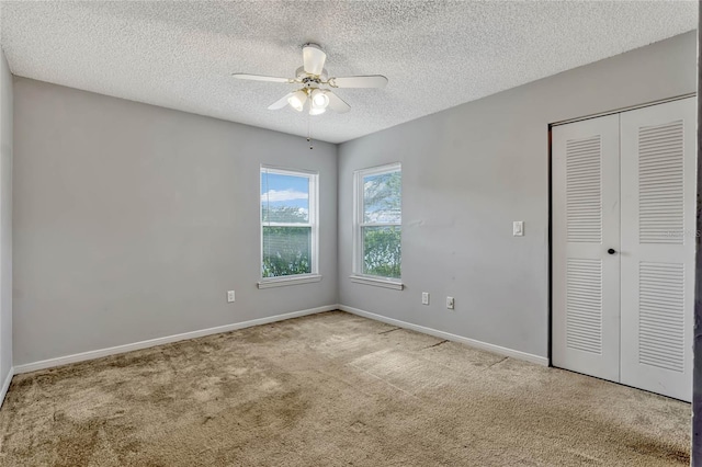 unfurnished bedroom featuring ceiling fan, light colored carpet, a textured ceiling, and a closet