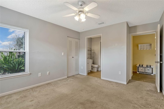 unfurnished bedroom with ensuite bathroom, ceiling fan, light carpet, a textured ceiling, and a closet