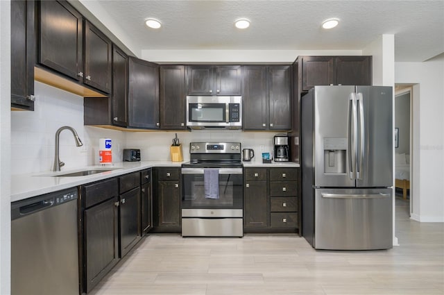 kitchen featuring appliances with stainless steel finishes, tasteful backsplash, sink, dark brown cabinetry, and light wood-type flooring