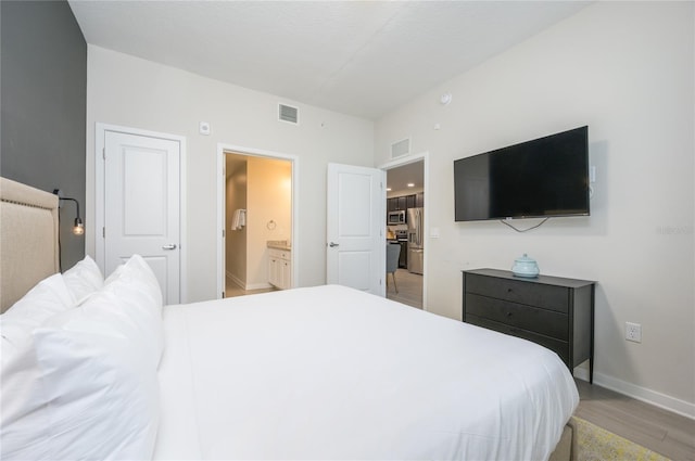 bedroom with stainless steel fridge with ice dispenser, ensuite bathroom, and light wood-type flooring